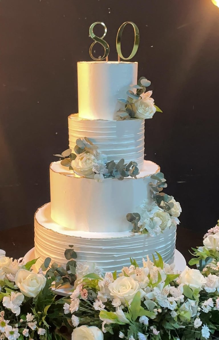 Bolo de aniversário decorado em camadas com flores brancas e verdes, celebrando 80 anos, ideal para