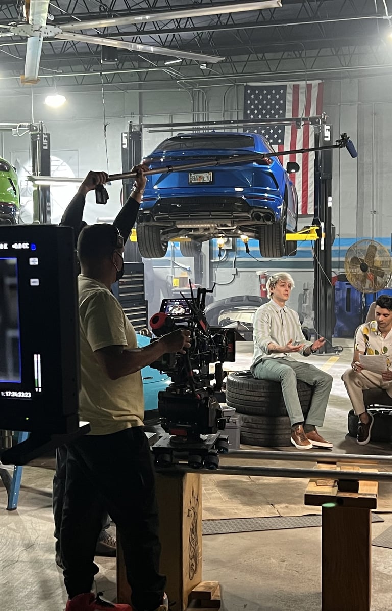 Professional film crew recording a video production in a car garage with exotic sports cars on lifts.