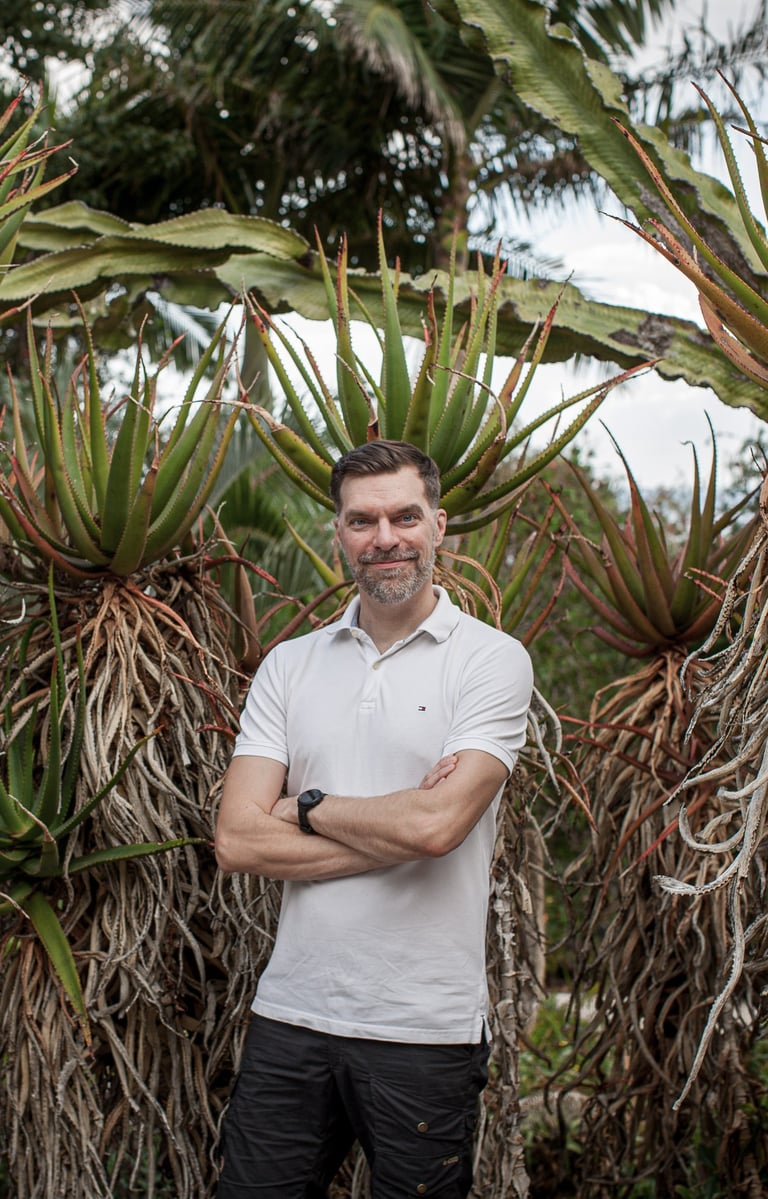 Man stands in a lush botanical garden surrounded by tall aloe and cactus plants, Madeira lifestyle and natural greenery.