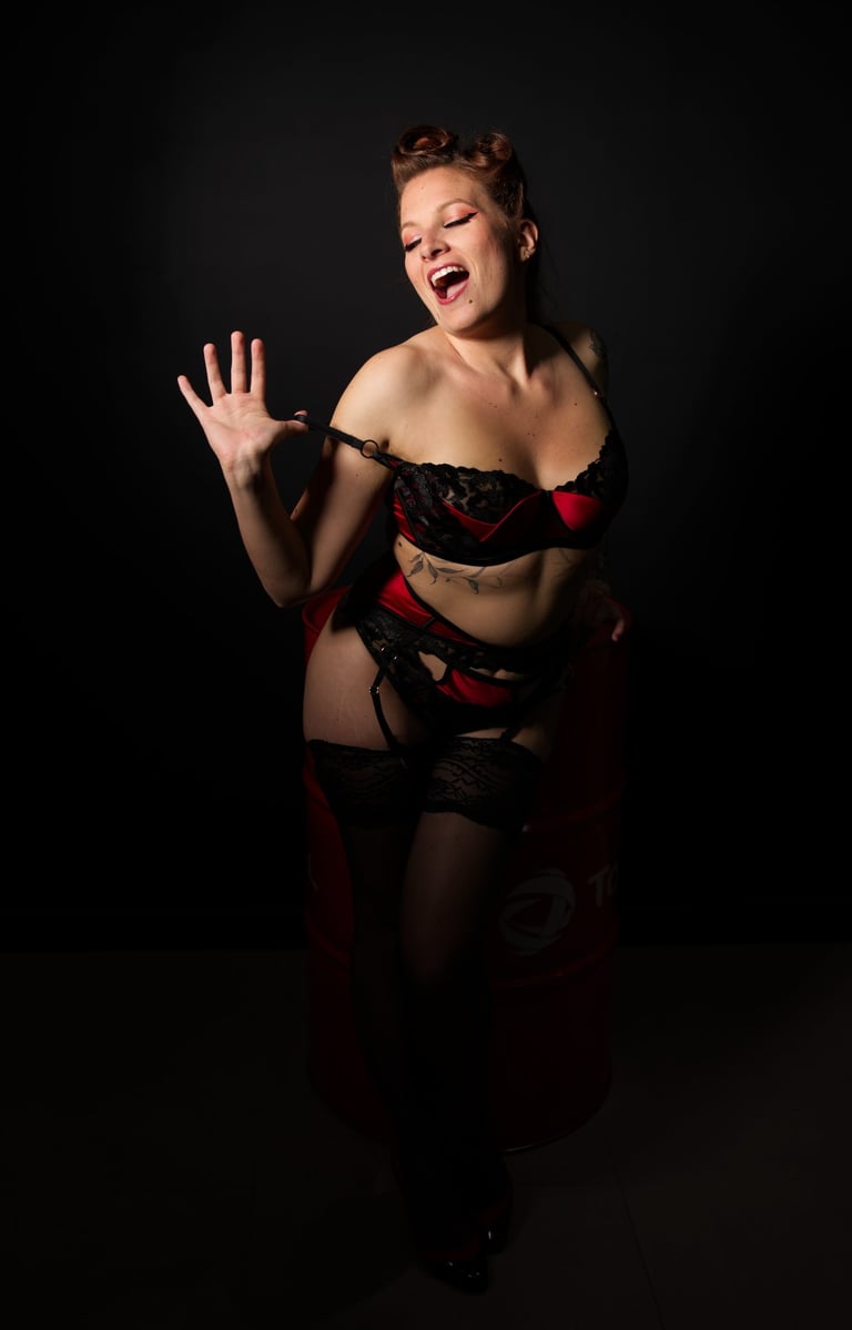 Glamour. Femme en lingerie rouge et noire qui se déshabille en souriant.
