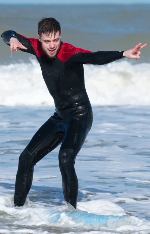 Une homme en combinaison en train de poser sur une planche de surf dans l'océan