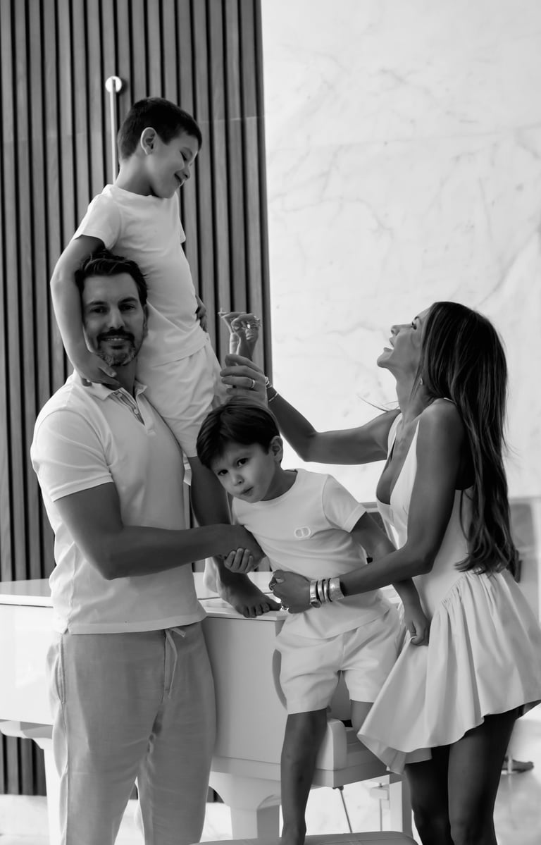 Black-and-white family photo of two parents playing with their sons indoors.