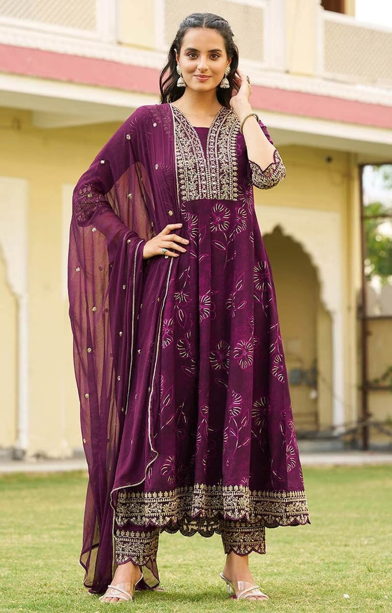 Woman wearing a purple Anarkali suit with gold embroidery and a matching sheer dupatta.