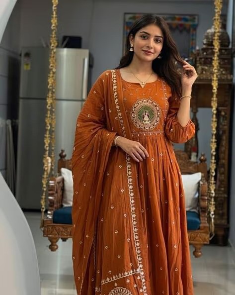 Woman wearing an elegant rust orange Anarkali suit with traditional Indian embroidery.