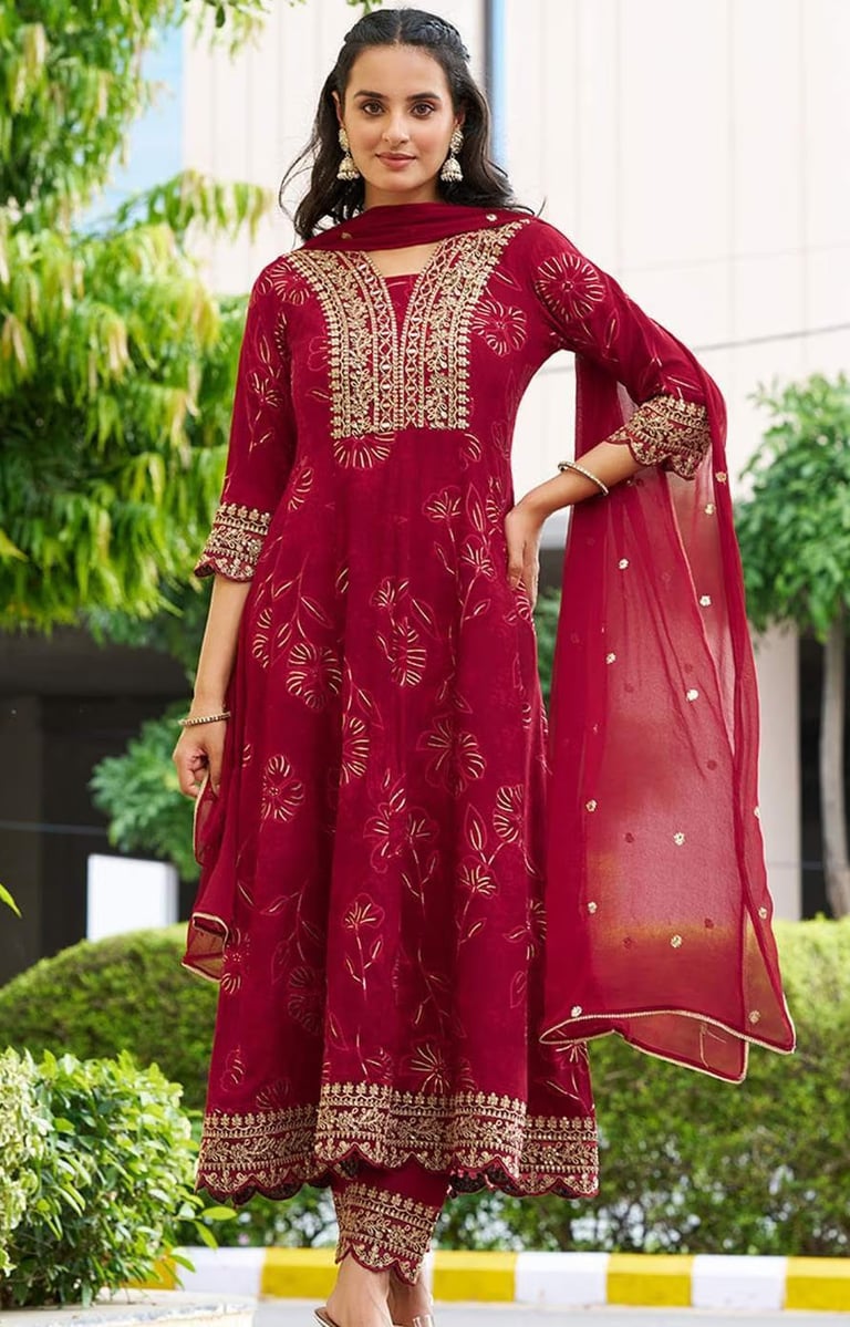 Woman wearing a maroon embroidered Anarkali suit with gold zari work and matching dupatta.
