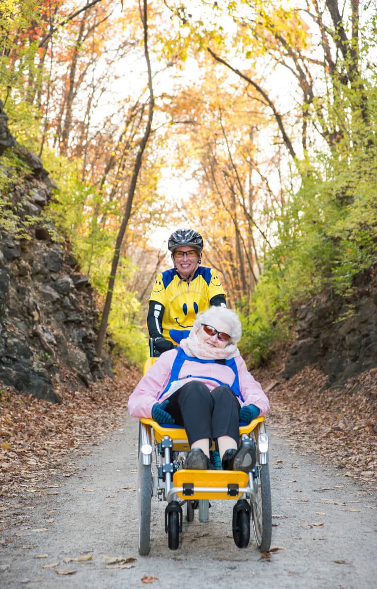 Two smiling people, one sitting in the giving rides bike, and one positioned above them pedaling