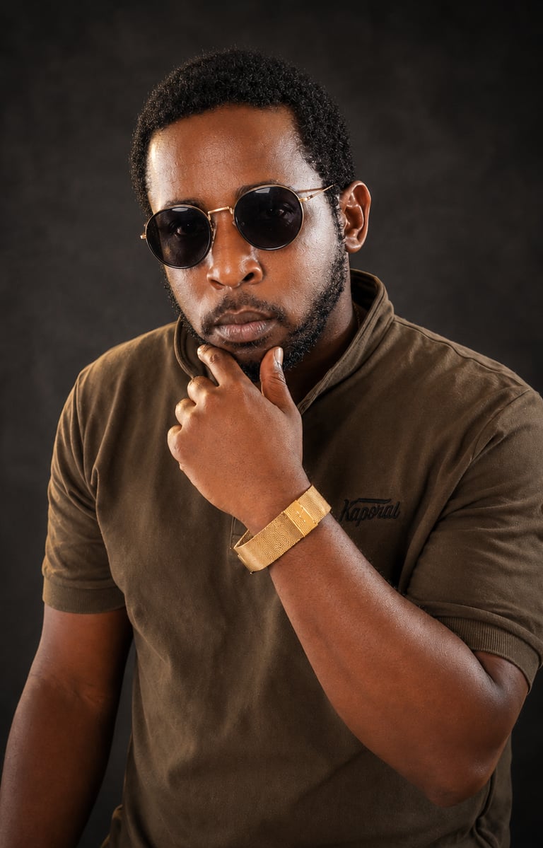 A stylish Ochomane wearing round sunglasses and a gold bracelet posing against a dark background.