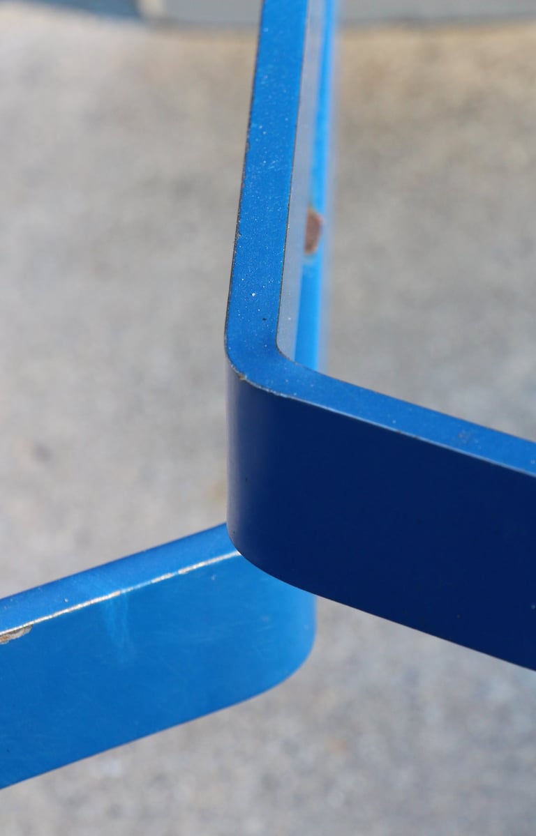 Two bright blue metal elements resembling hockey sticks set against blurry background..