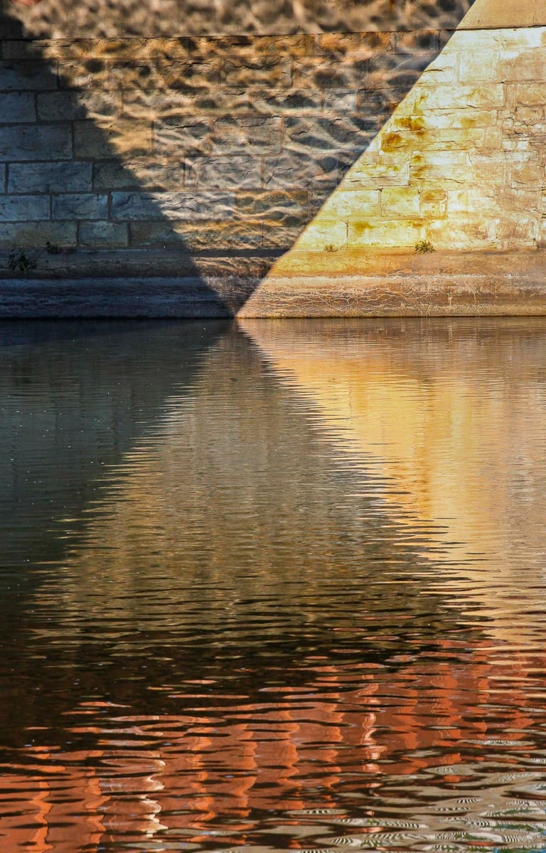 Riverbank casting beautiful multicolor geometric shadows on the water surface & wall.