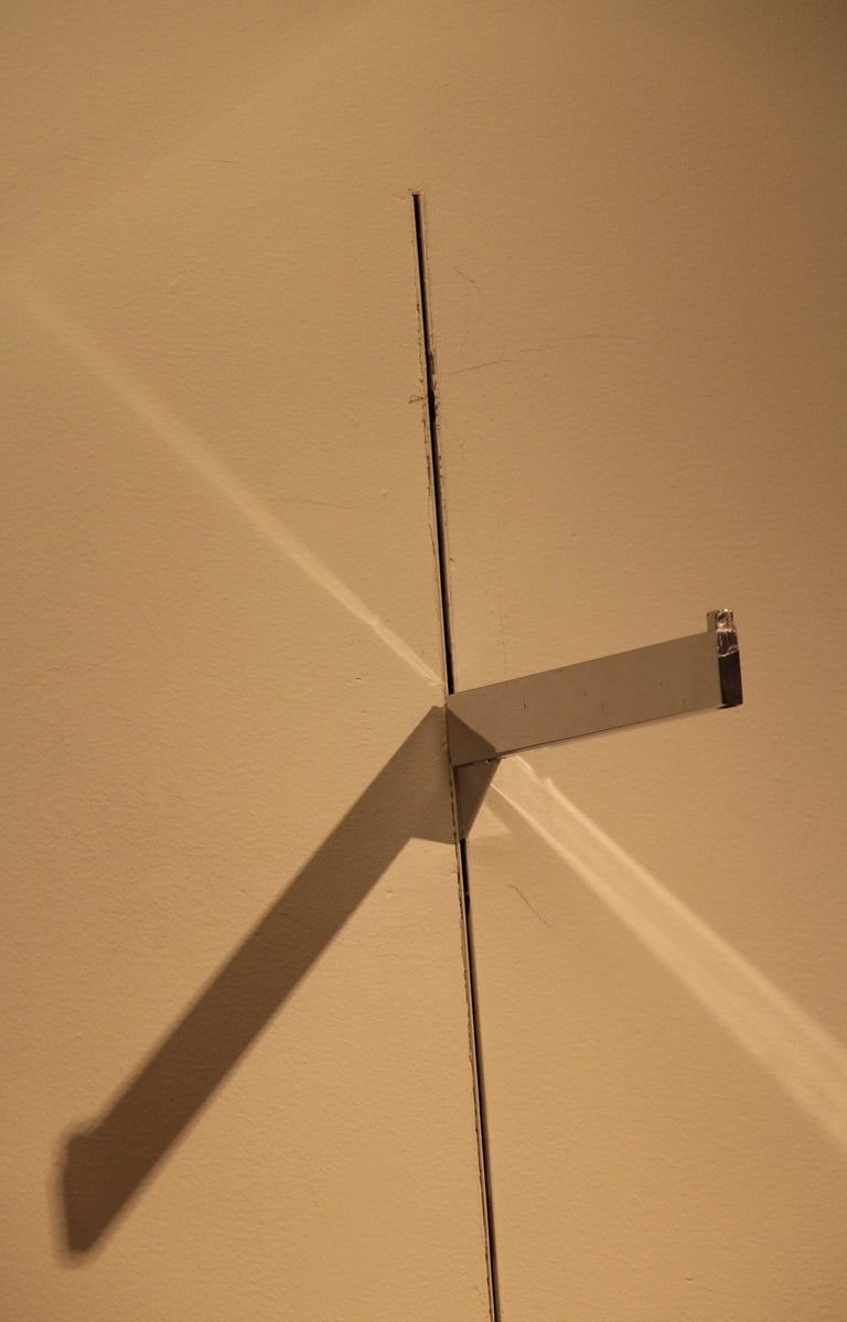 A beige wall with a protruding shelve bracket casting multiple shadows.