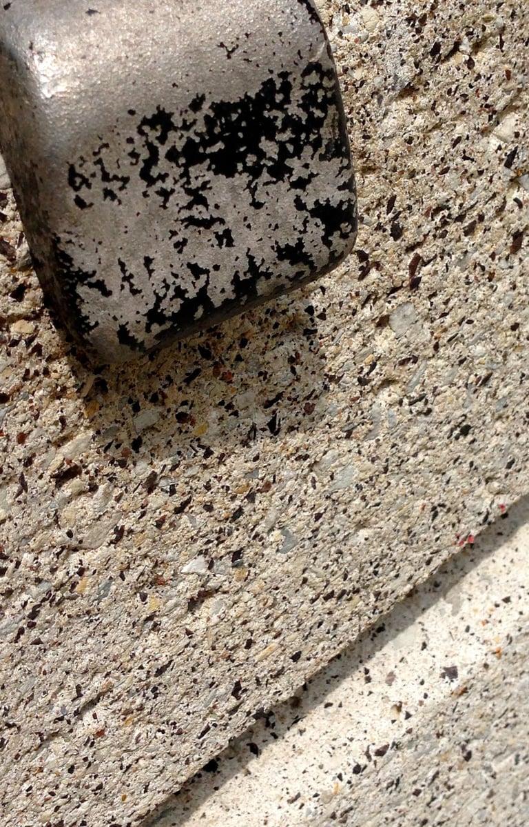 Bulky steel bent bracket, stripped off black paint, holding porous concrete edge.