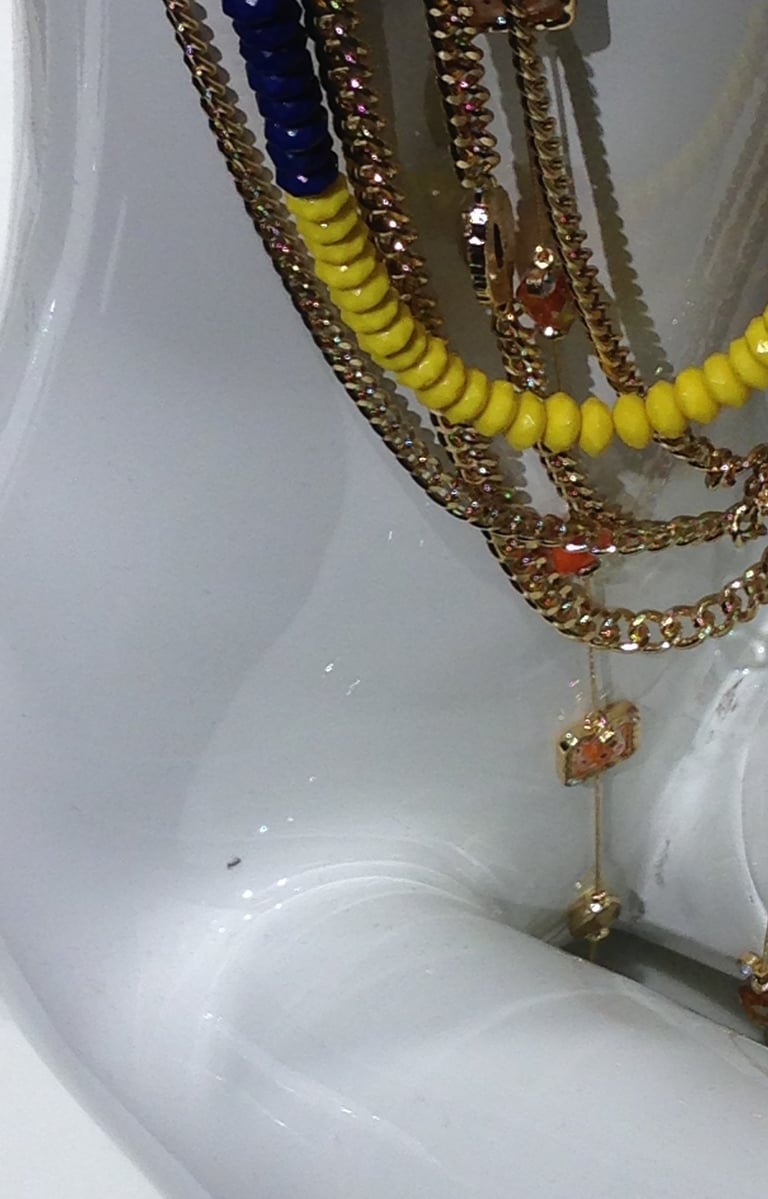 White shiny reflective female manekin with gold chains and blue-yellow plastic neckless.  