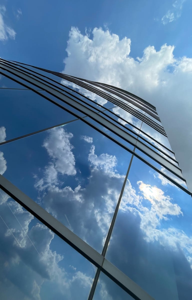 Looking up into the blue cloudy sky through reflection in a glass-steel building.