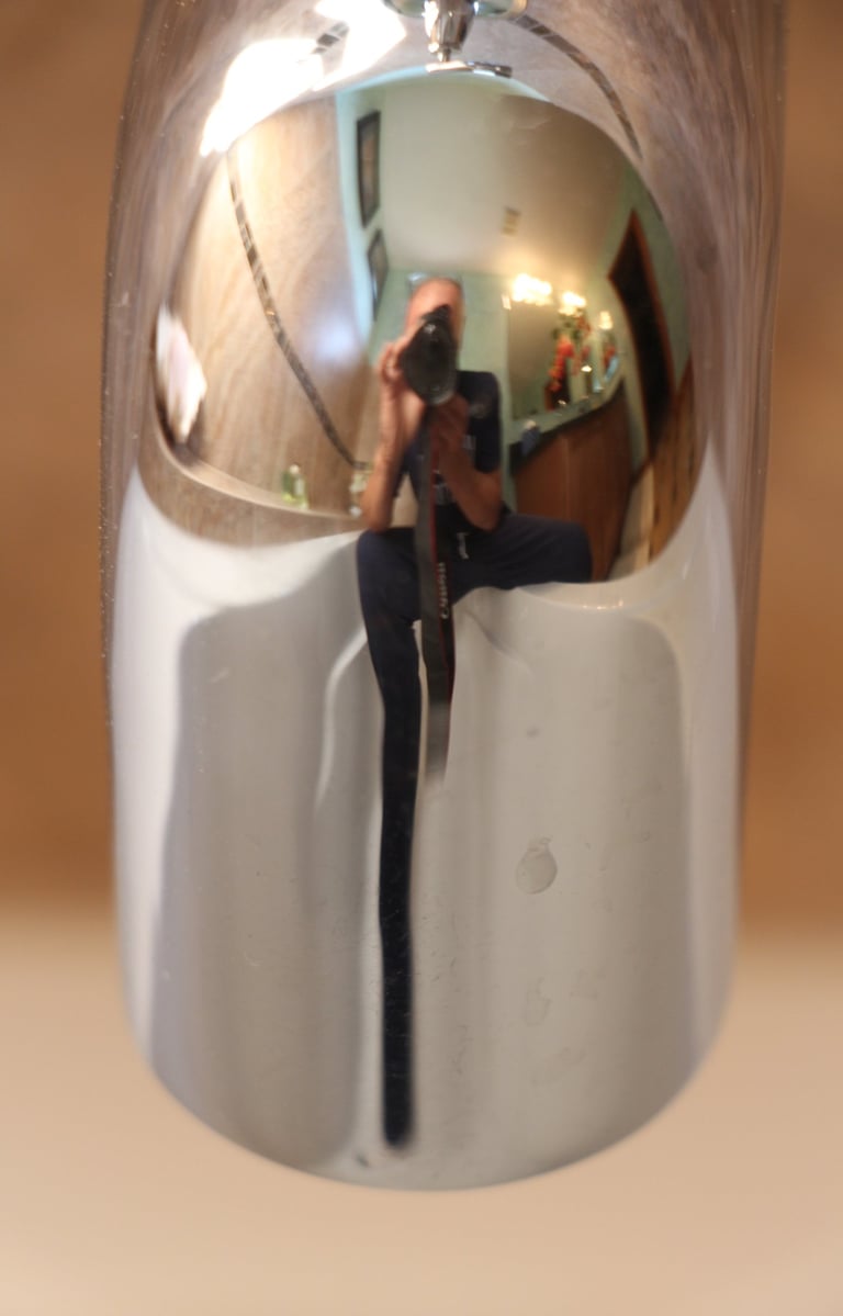  An image showing a mirror reflection of a male figure sitting with a camera on a white tub.