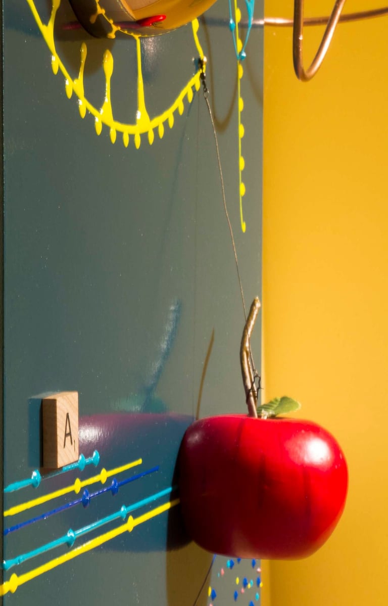 Red apple attached to dark green shiny surface with colorful marks & wooden letter A. 