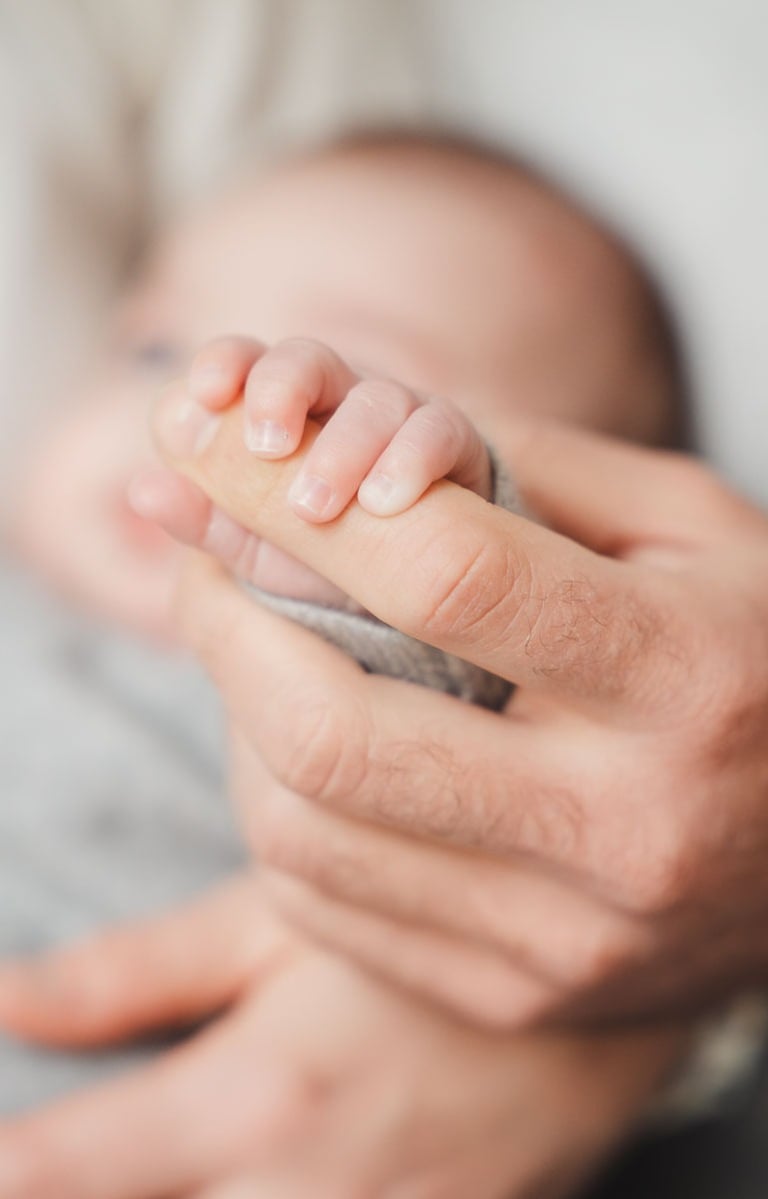 Photographe naissance Paris : gros plan sur la main du bébé attrapant le doigt de son père