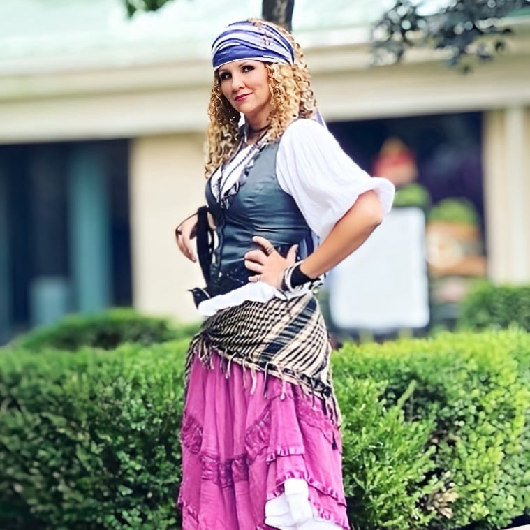 Woman in a pirate costume with a purple skirt and bandana posing outdoors.