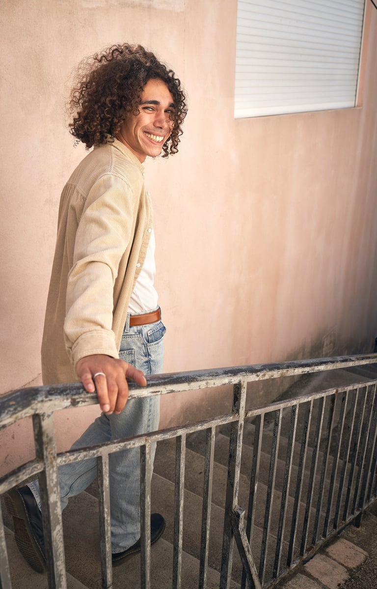 A man with long curly hair smiling at the camera on the stairs of Notre-Dame de la Garde