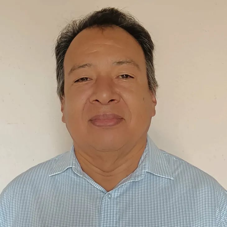 Professional headshot of a middle-aged man with short dark hair wearing a light blue checkered shirt.