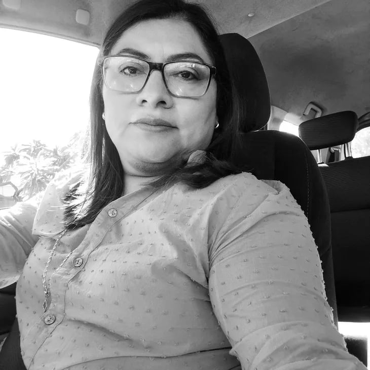 A black and white portrait of a woman wearing glasses and a polka dot shirt sitting inside a car.
