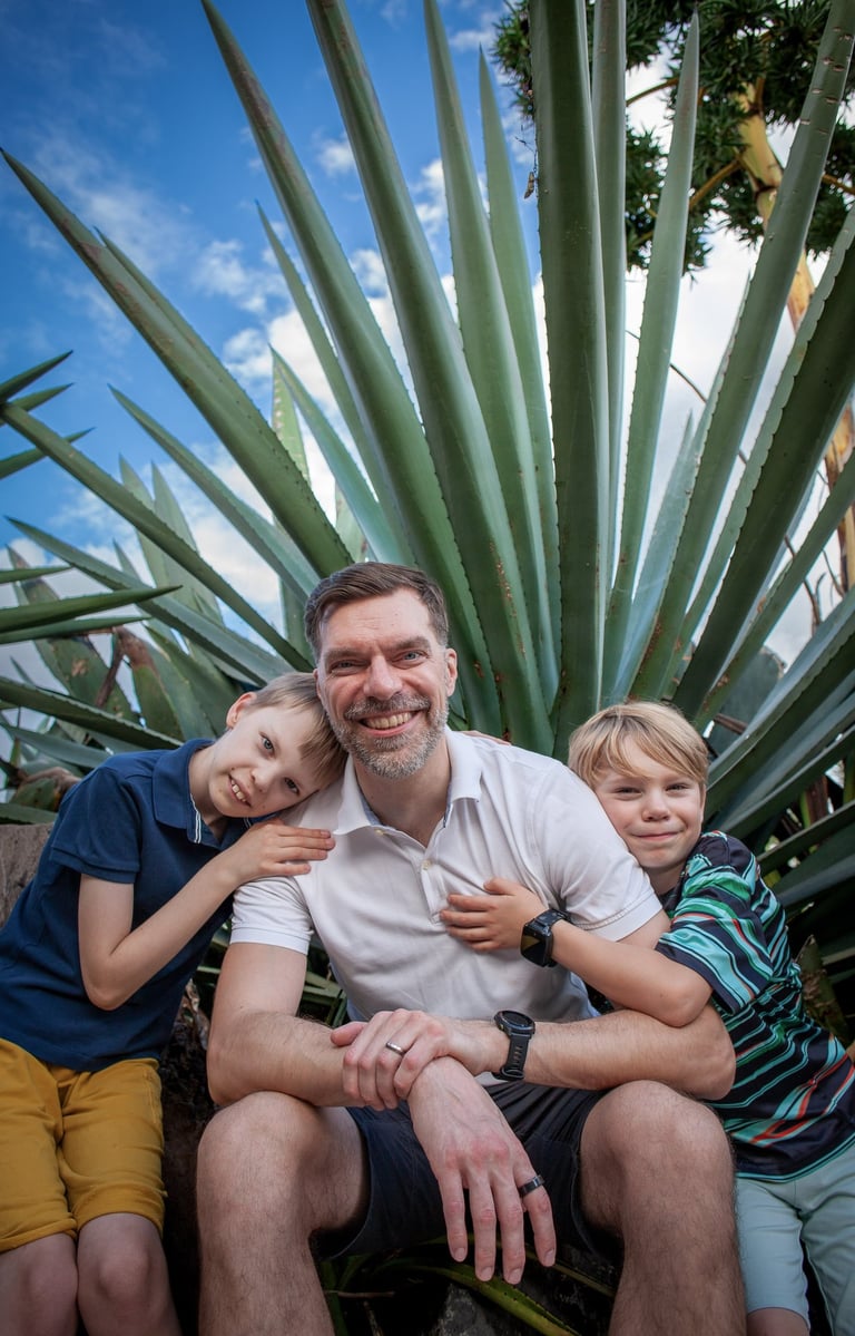 Father sits with his two sons in front of dramatic agave plants in Madeira botanical garden, lifestyle family portrait.