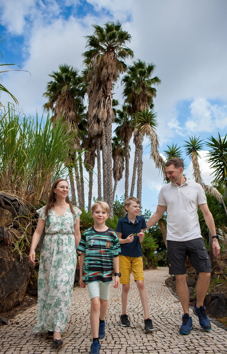 Family walks together along a palm-lined path in a tropical garden, sunny day in Madeira, relaxed lifestyle vibe.