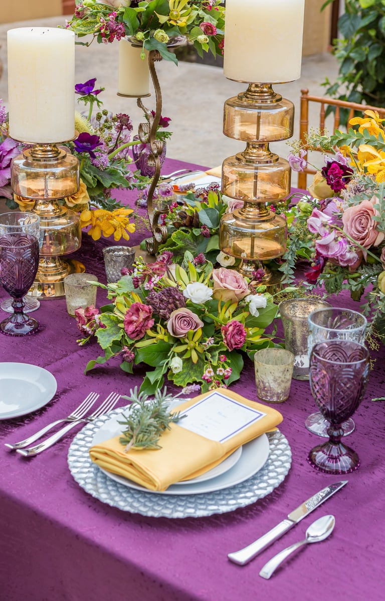 beautiful wedding tablescape with purple linens and bold colored flowers, candles and purple glasses