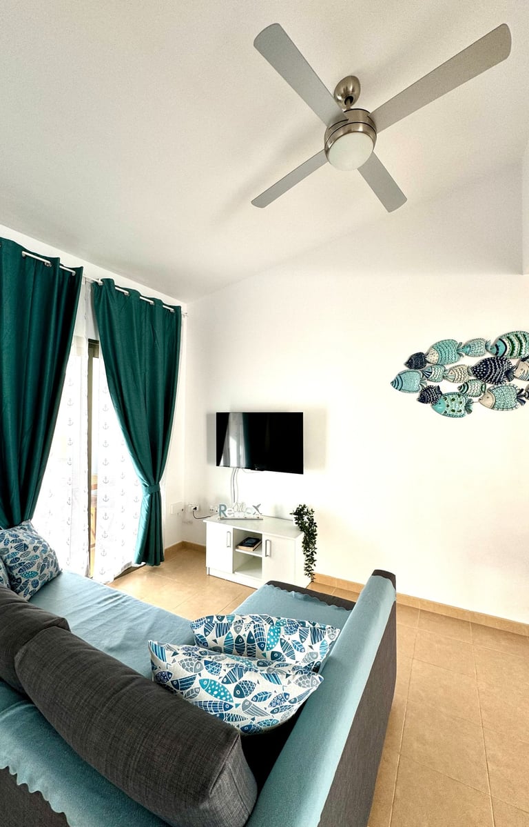 Modern living room with teal curtains, a blue sofa, fish wall decor, and a ceiling fan.