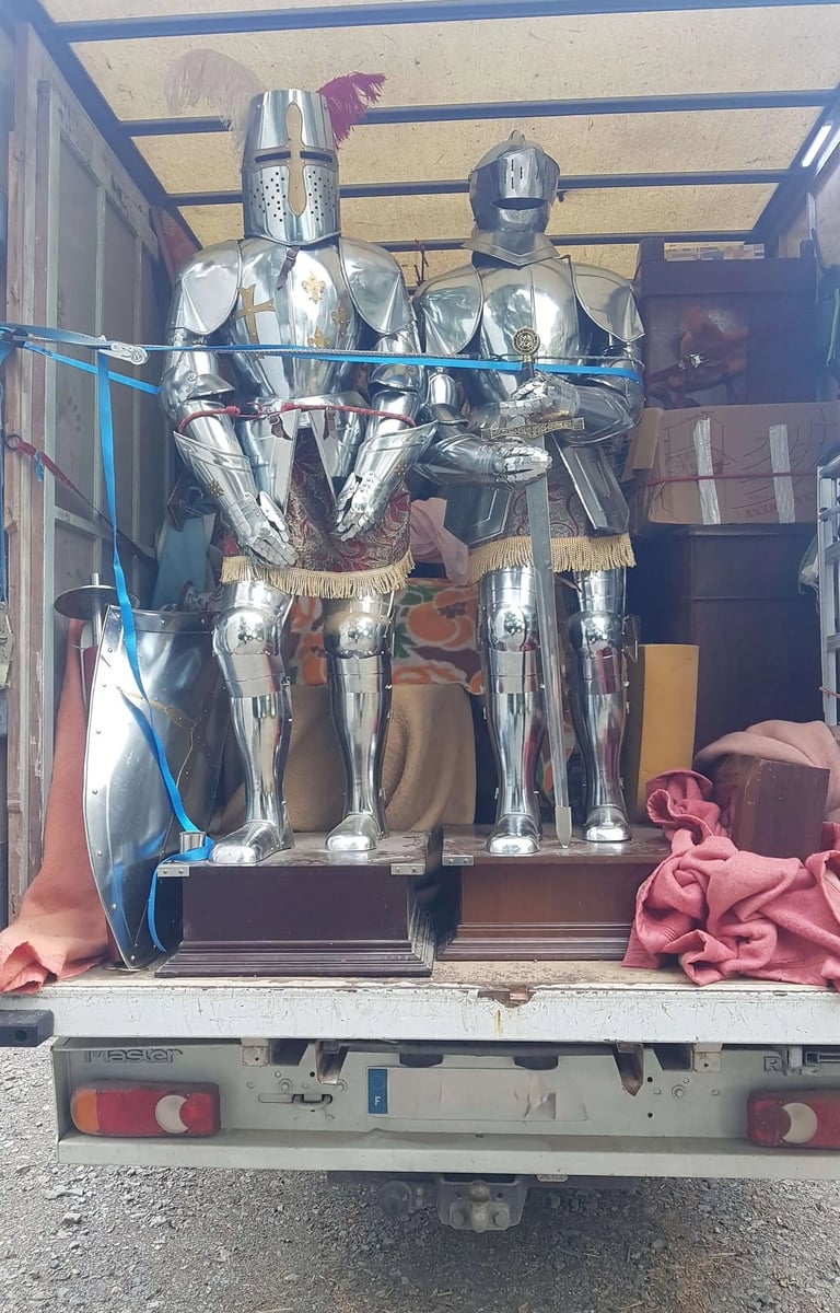 Brocante Lepeltier - Un camion transportant deux armures médiévales à l'arrière, sur un fond urbain.