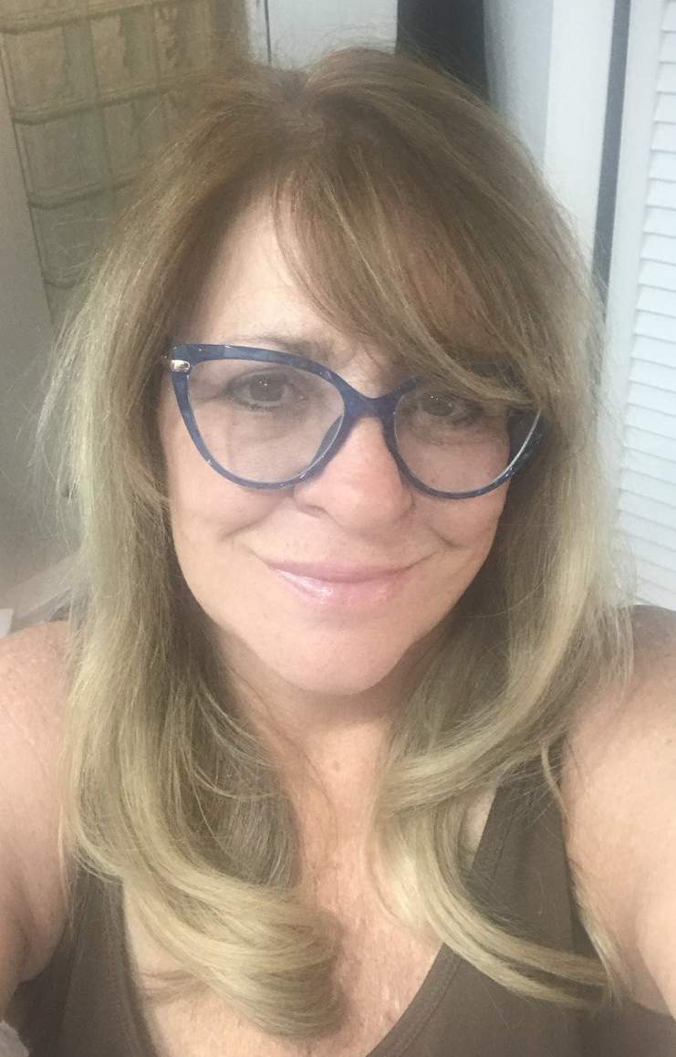 A smiling woman with blonde hair wearing stylish blue cat-eye glasses.