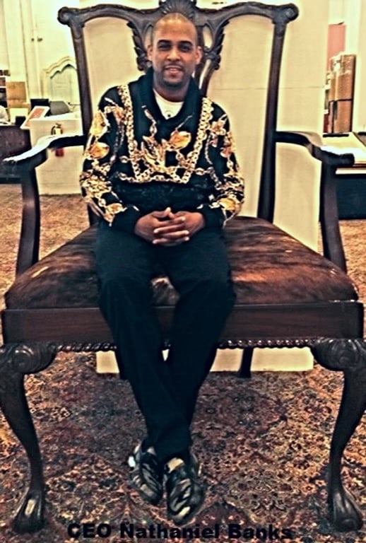 CEO Nathaniel Banks sitting on an oversized vintage throne chair wearing a designer gold chain print hoodie.