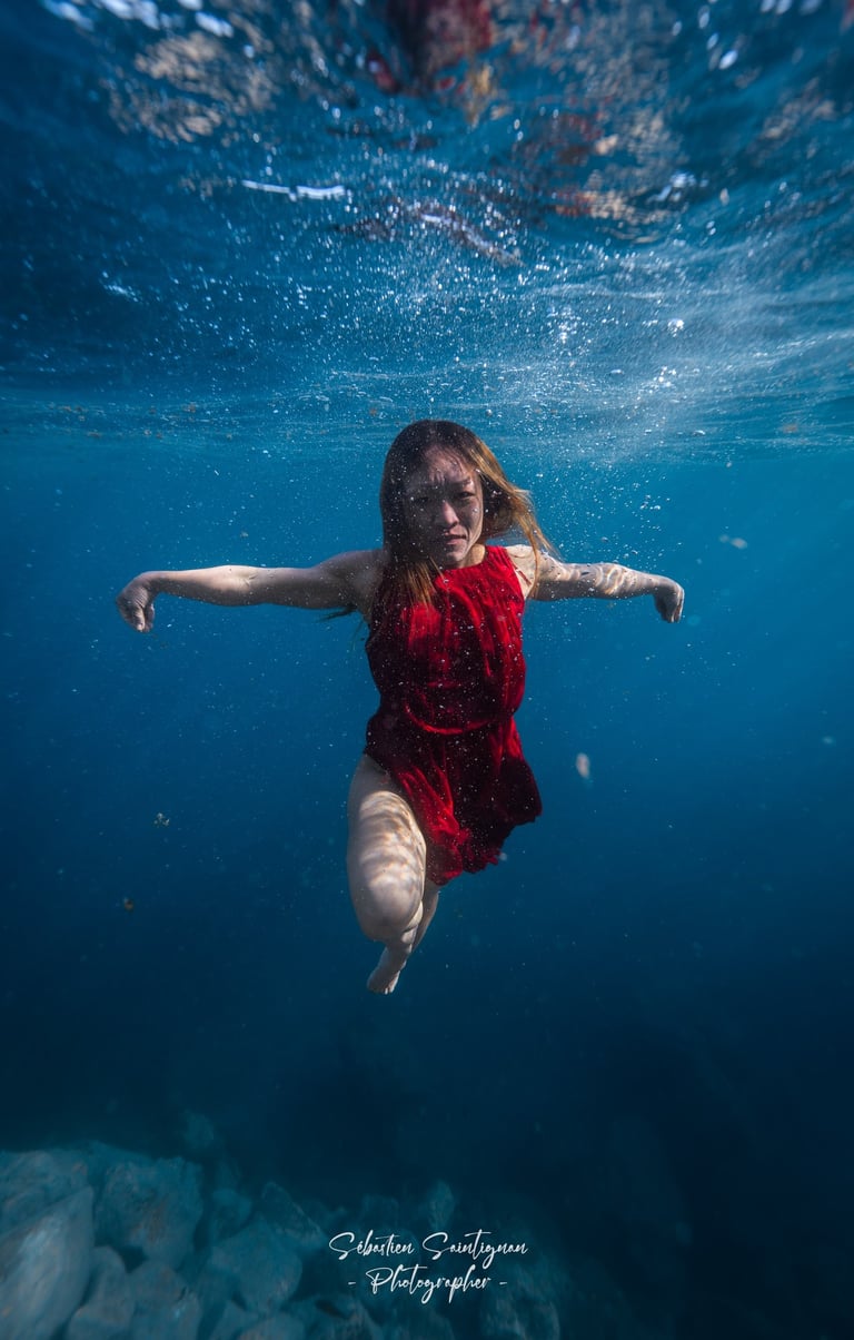 Model in red dress dancing underwater. Photo taken by Sébastien Saintignan 