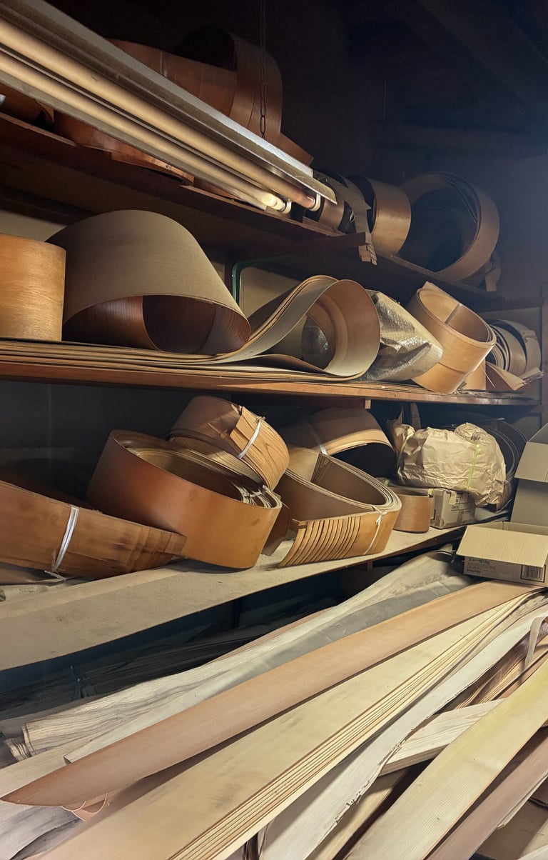 Curved wood veneer sheets and timber planks stored on shelves in a woodworking workshop.