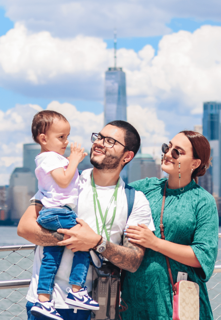 Happy family with toddler posing in front of the One World Trade Center and New York City skyline.