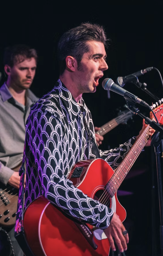 Live performance in Brighton featuring Olly Williams singing and playing guitar on stage with colourful lighting.