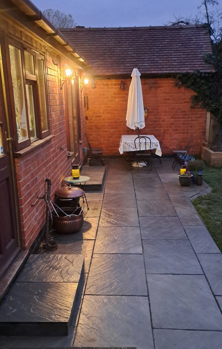 Illuminated backyard patio with grey slate flagstone tiles and a small outdoor dining table.