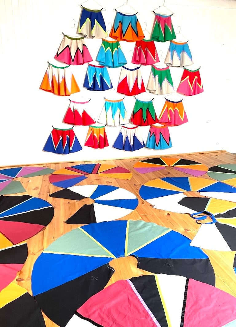 Handmade colorful circle skirts hanging on a wall and spread across a wooden floor in a sewing studio.