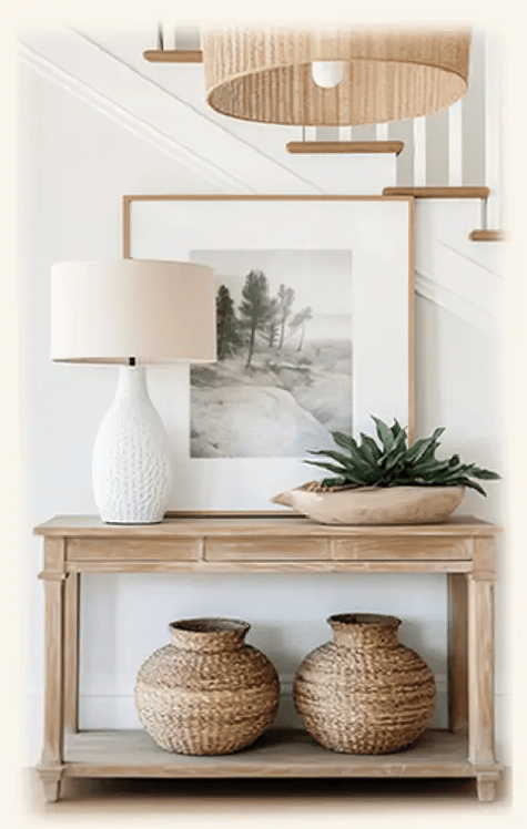 entrée intemporelle, console bois clair, pot en rotin dessous, plante verte, lampe blanche et tableau  dessus, suspension en 