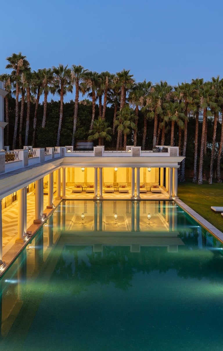 Luxury villa with illuminated outdoor pool, palm trees, and modern poolside lounge at twilight.