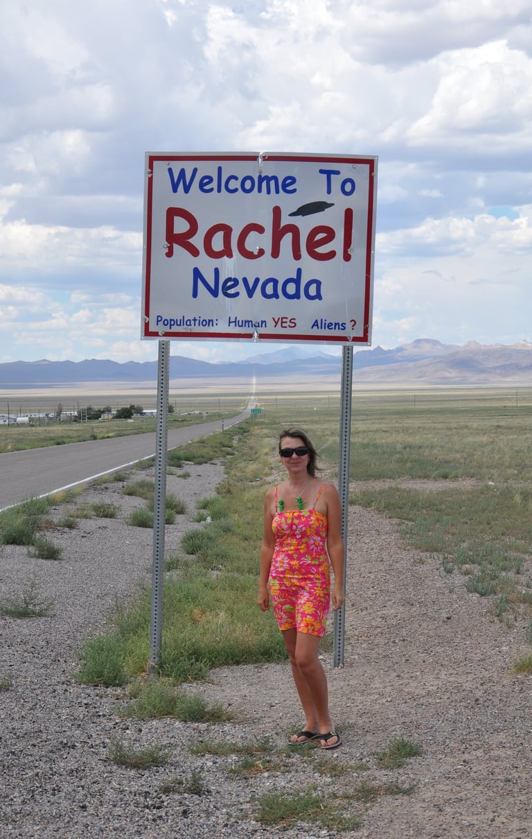 a woman standing in front of a welcome sign for Rachel, Nevada