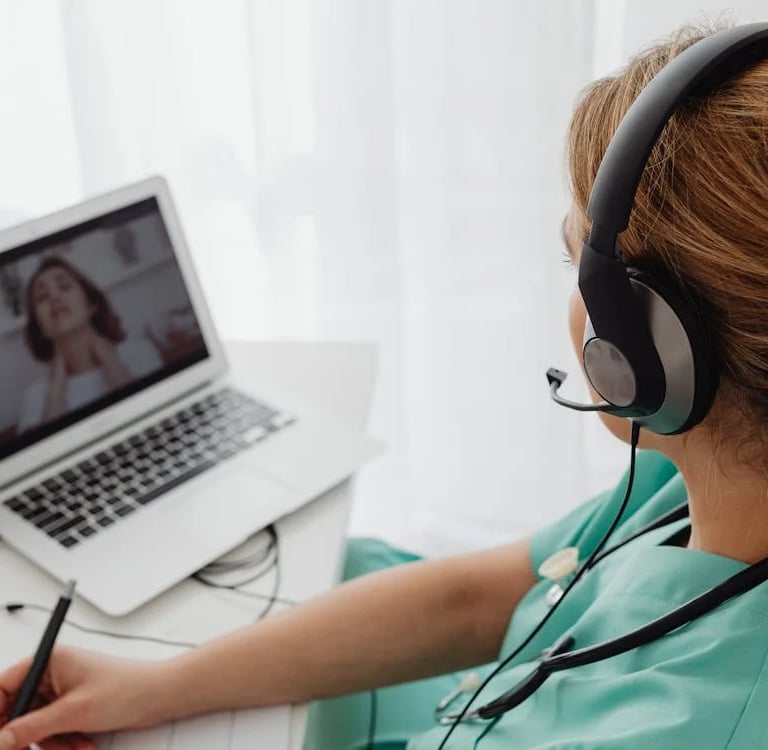 a woman in a green scrub suit is sitting at a desk with a laptop and