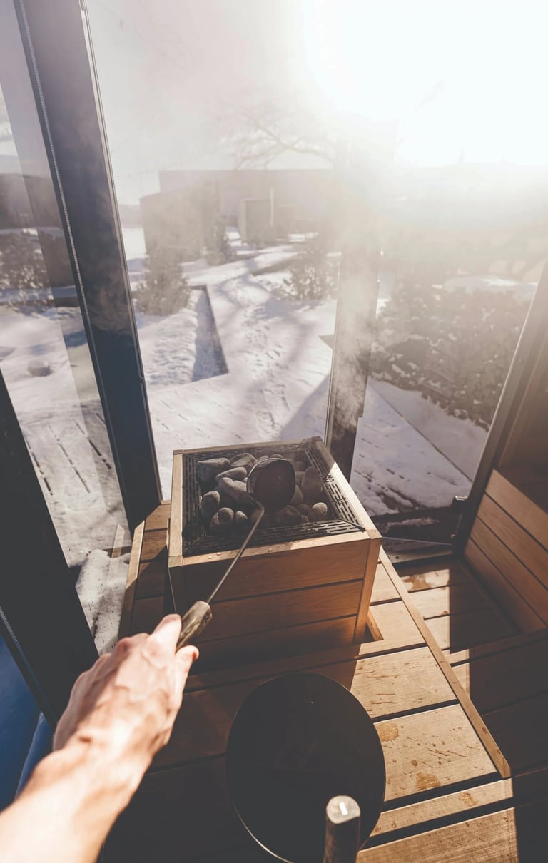 Pouring water on hot sauna stones inside a cedar Outdoor sauna Ontario with winter sunlight