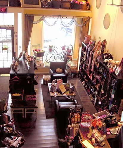 Cozy knitting shop interior with shelves of colorful yarn skeins, seating area, and boutique craft supplies.