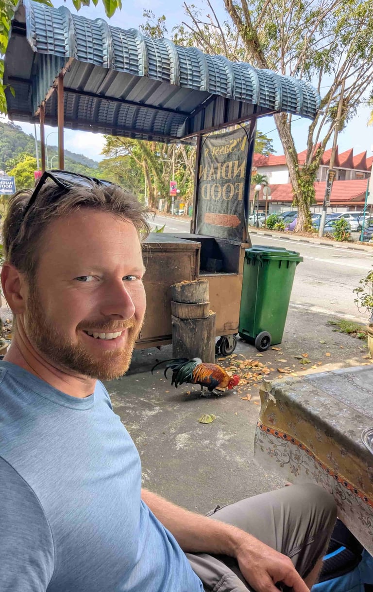 The blog's author Don sitting near a rooster in a restaurant in Penang, Malaysia.