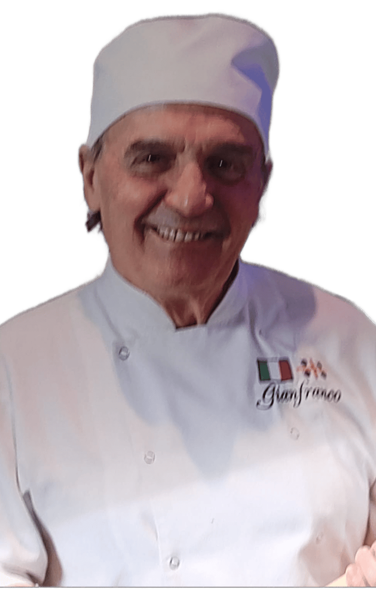 Smiling Italian chef Gianfranco wearing a professional white chef coat and toque hat.