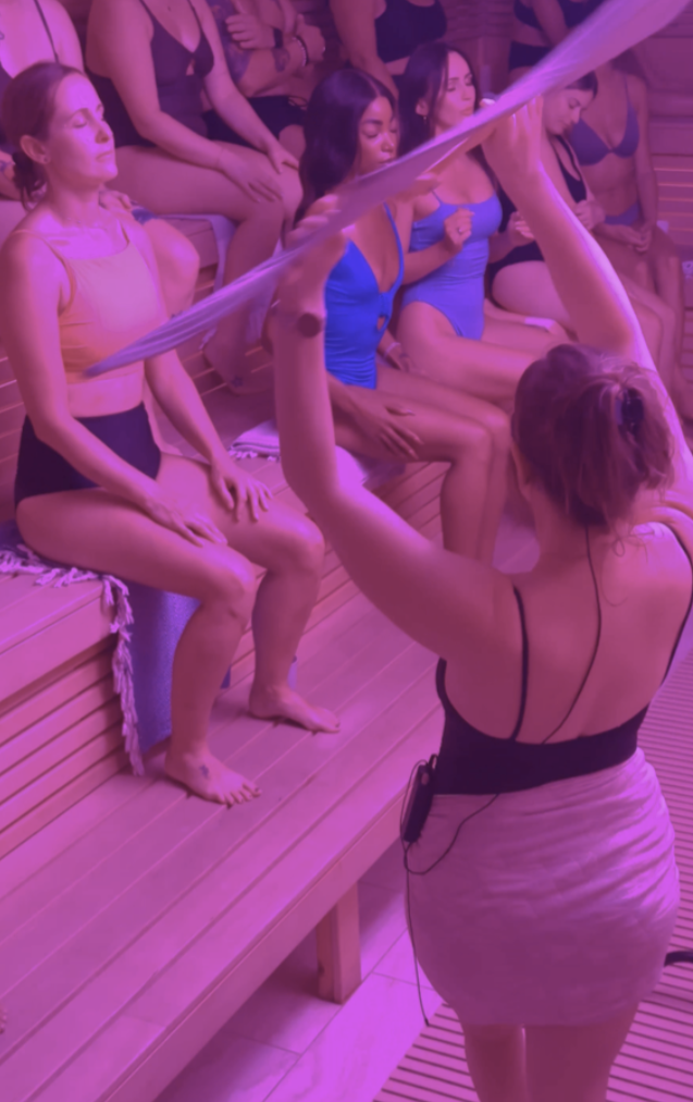 A group of women in a Finnish sauna participating in an Aufguss steam ritual with a towel.