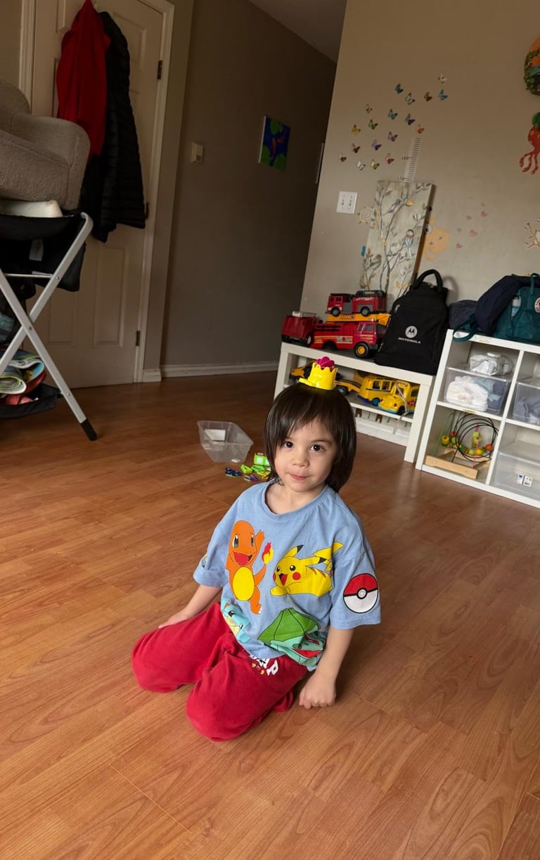 A young boy in a Pokemon shirt sits on a wooden floor in a playroom.