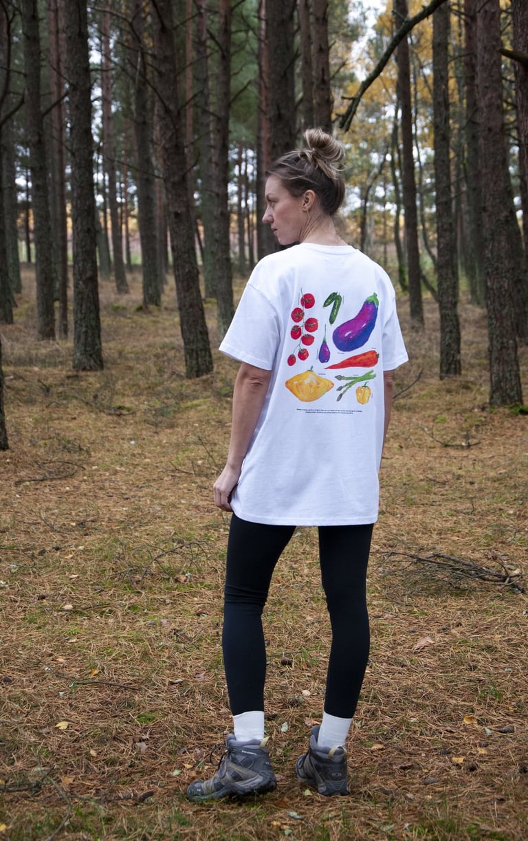 a woman in a white shirt and handmade vegetable illustration and black leggings standing in a forest