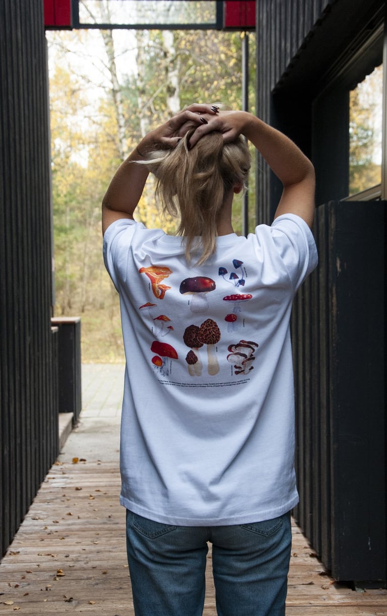 a woman in a white shirt and handdrawn mushroom illustration and jeans standing on a wooden deck