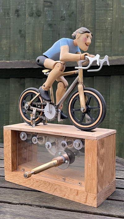 Articulated carved wooden cyclist on brazed metal miniature road bike, on base with visible cogs